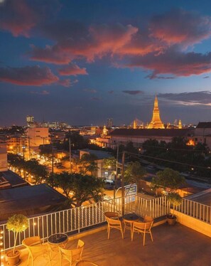 Terraço no telhado com mobiliário para área externa, vista da paisagem urbana ao entardecer e um edifício imponente ao fundo.