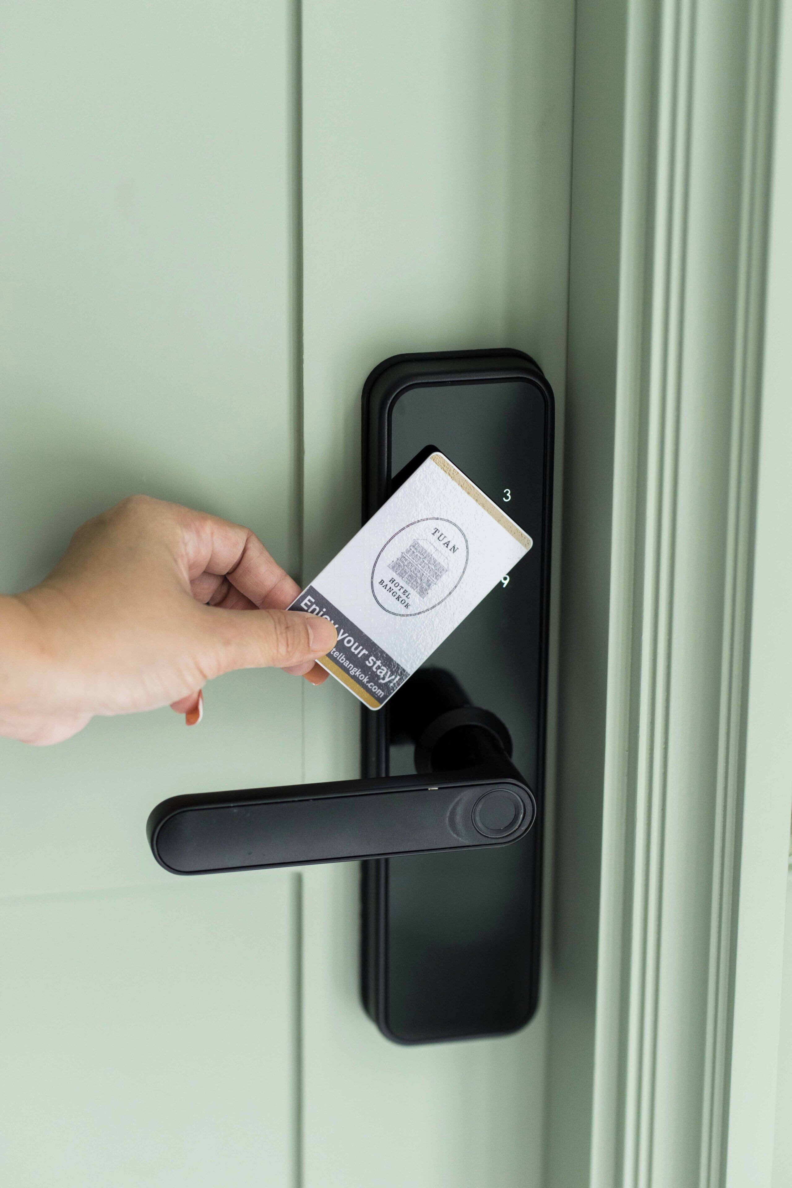 A hand holding a card with a QR code and text, placed on a door handle.