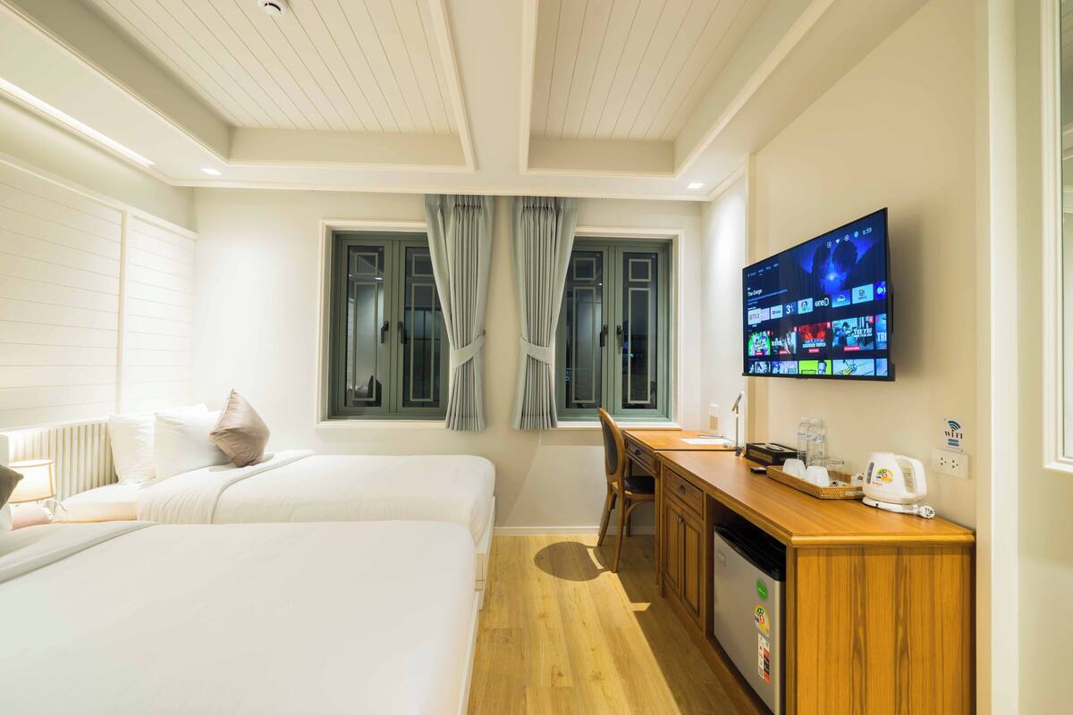 Une chambre d’hôtel avec deux lits, un bureau, un téléviseur fixé au mur et une fenêtre avec des rideaux.