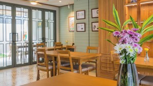 A dining area with wooden tables and chairs, a vase with flowers, and a wall with framed pictures. - TUAN Hotel Bangkok near Wat Arun (Bangkok)