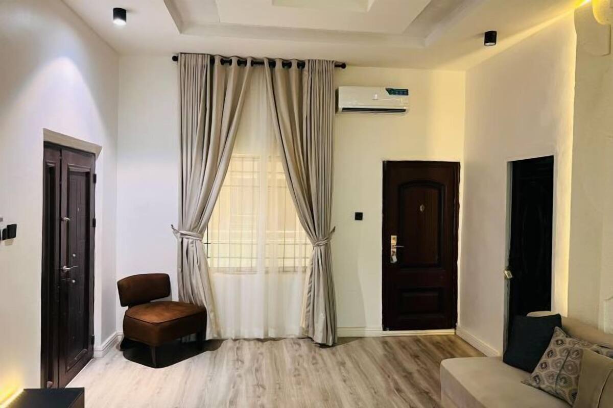 A room with a wooden floor, a sofa, a chair, a door, and a window with curtains.