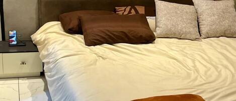 A bed with a headboard, pillows, and a bedside table with a phone.