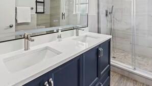 Un baño moderno con un espejo grande, lavamanos dobles y una ducha con cerramiento de vidrio.