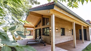 A wooden cabin with a covered deck, large windows, and a sliding door. - Komfortables Ebenerdiges Chalet im Vital Camp Bayerbach (Bayerbach)