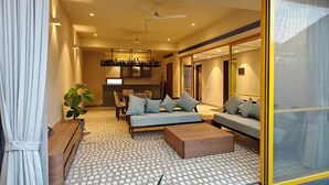 A modern living room with a sofa, coffee table, and a dining area with chairs and a table. - Touchwood Bliss Resort - Igatpuri (Igatpuri)