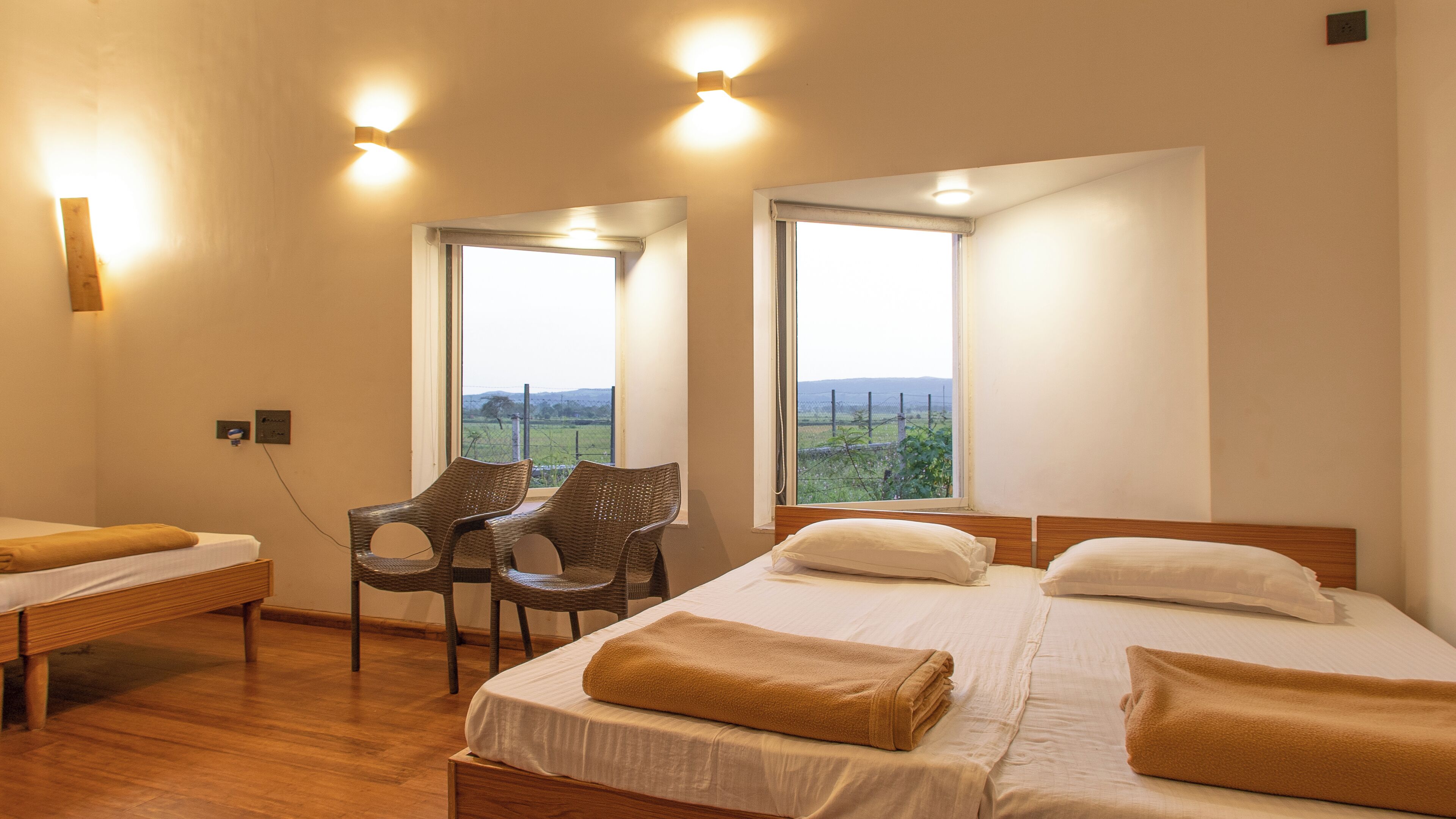 Un dormitorio con dos camas, una silla y dos ventanas que dan a un paisaje rural.