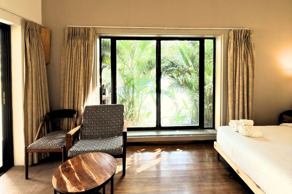 A room with a bed, a chair, a round table, and a large window with curtains.