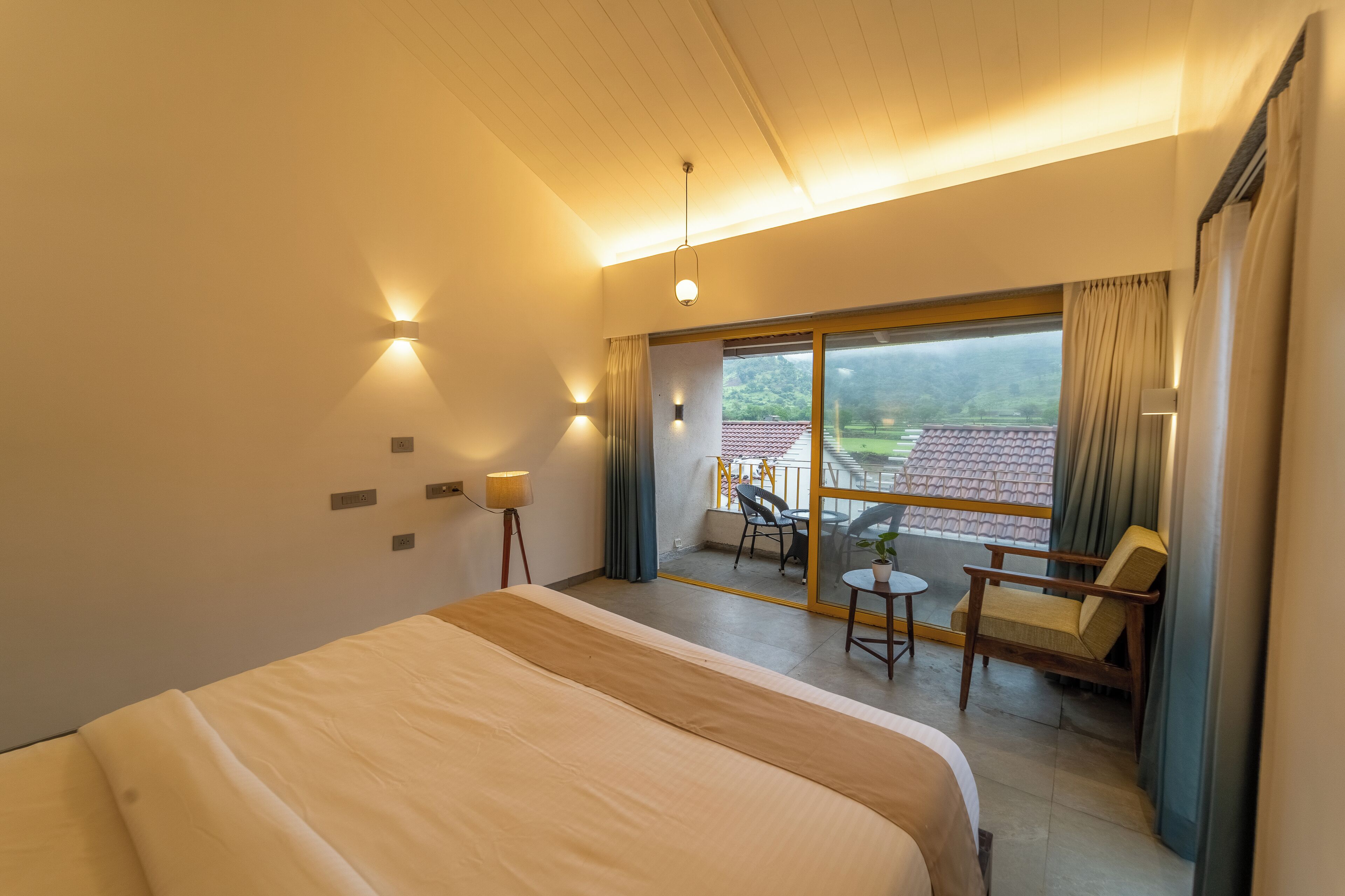 A hotel room with a large bed, a balcony with a table and chairs, and a view of a red-tiled roof.