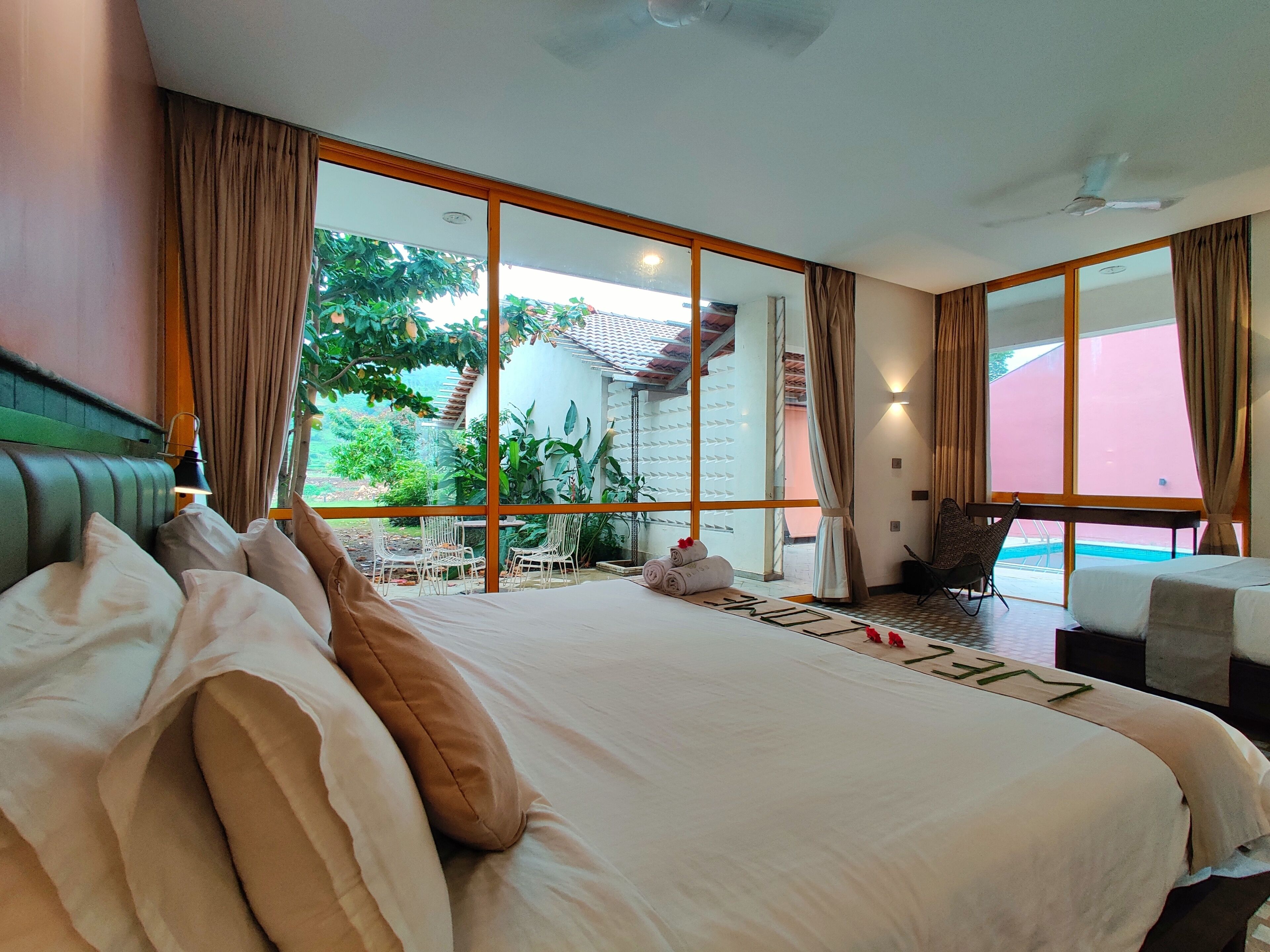 Ein geräumiges Schlafzimmer mit einem großen Bett, Blick auf einen Swimmingpool und einem Balkon mit Sitzgelegenheit.