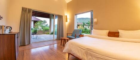 A hotel room with a large bed, a desk with a chair, a small table, and a view of the outdoors.