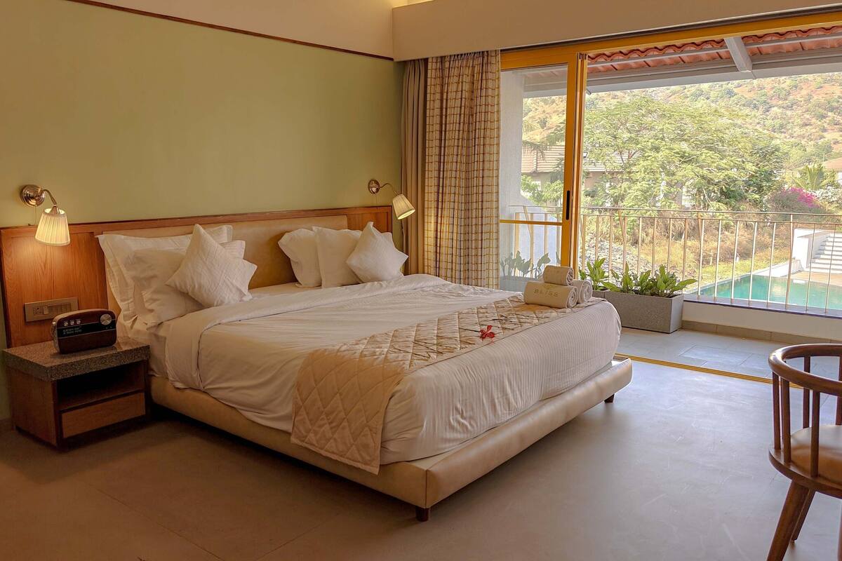 A bedroom with a large bed, bedside lamps, a radio, and a view of a swimming pool.