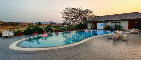 A swimming pool with a curved edge, surrounded by potted plants and outdoor furniture.