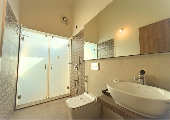 Un baño con un lavamanos grande, una ducha con puerta de cristal y un espejo sobre el lavamanos.