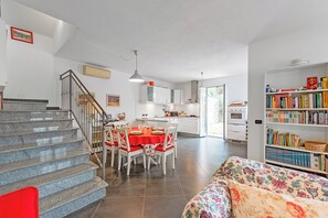 Une cuisine moderne avec des meubles blancs, une table à manger pour quatre personnes et un escalier menant à l’étage supérieur.