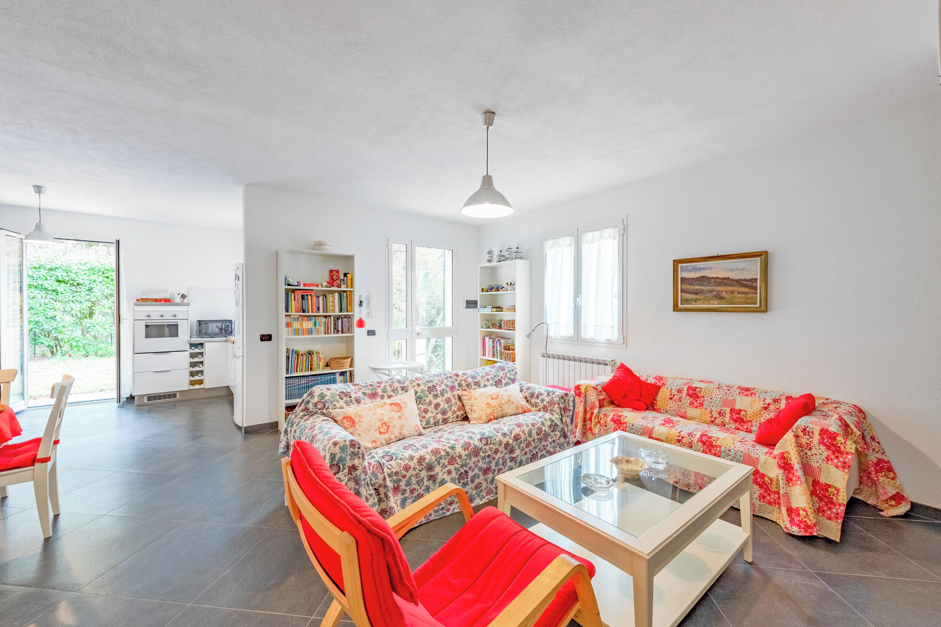 A modern living room with a sofa, chairs, a coffee table, and a kitchen area visible through an open door.