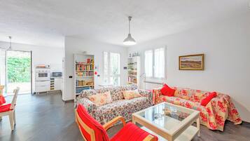 A modern living room with a sofa, chairs, a coffee table, and a kitchen area visible through an open door.
