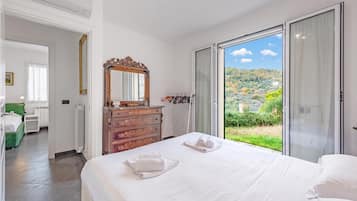 A hotel room with a large bed, a dresser, a mirror, and a view of a green landscape through a sliding glass door.