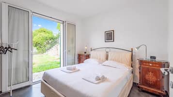 A bedroom with a bed, a nightstand, a lamp, a dresser, and a sliding glass door leading to a garden.