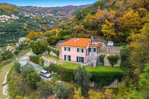 A hillside house with a stone facade, green shutters, and a red roof.
