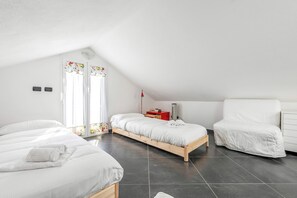 Un dormitorio con techo inclinado, dos camas, una mesita de noche, una silla y una ventana con cortinas.