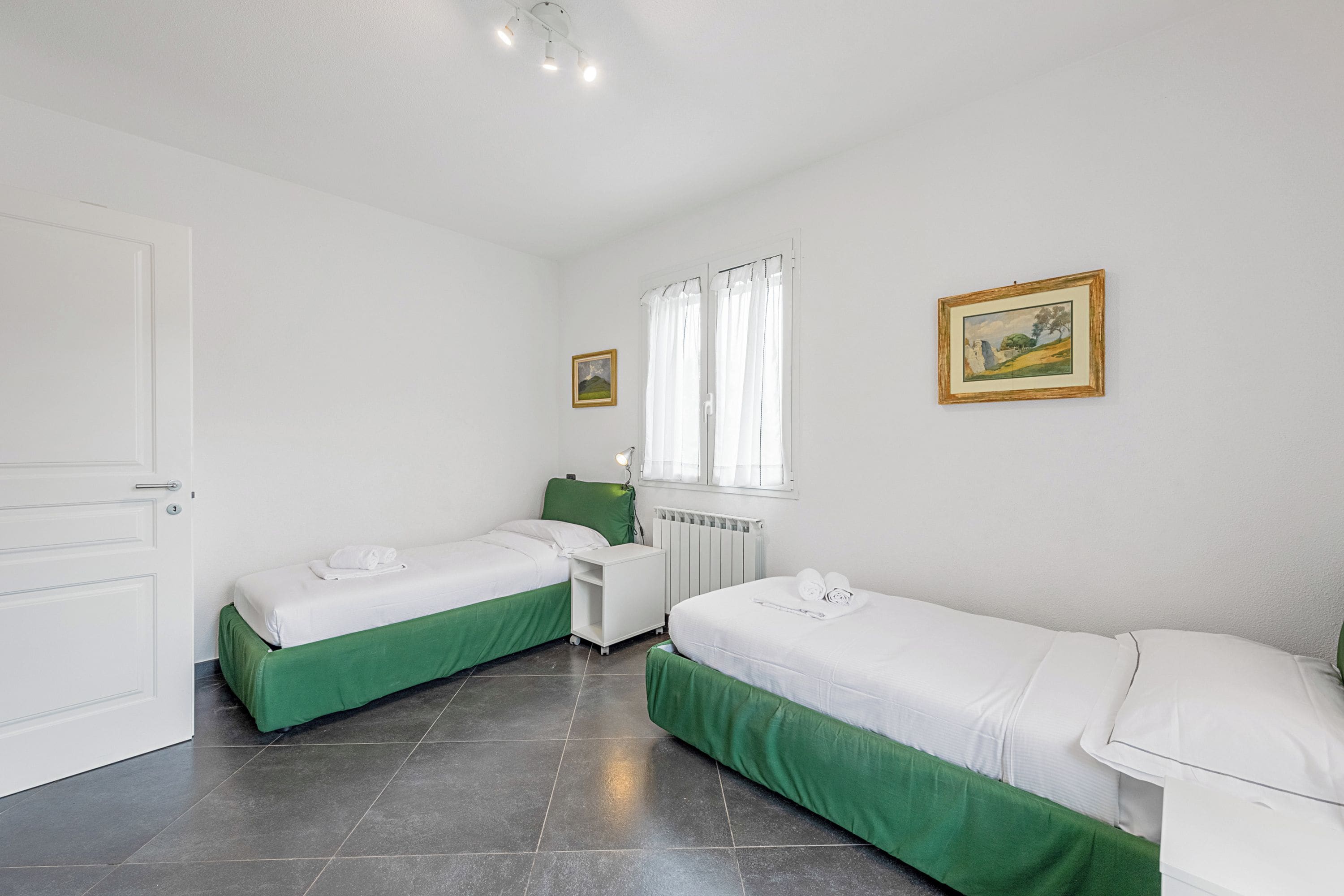 Una habitación limpia y bien iluminada con dos camas individuales, un escritorio pequeño blanco y un radiador.