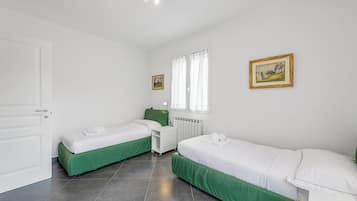 Ein sauberes, helles Zimmer mit zwei Einzelbetten, einem kleinen weißen Schreibtisch und einem Heizkörper.