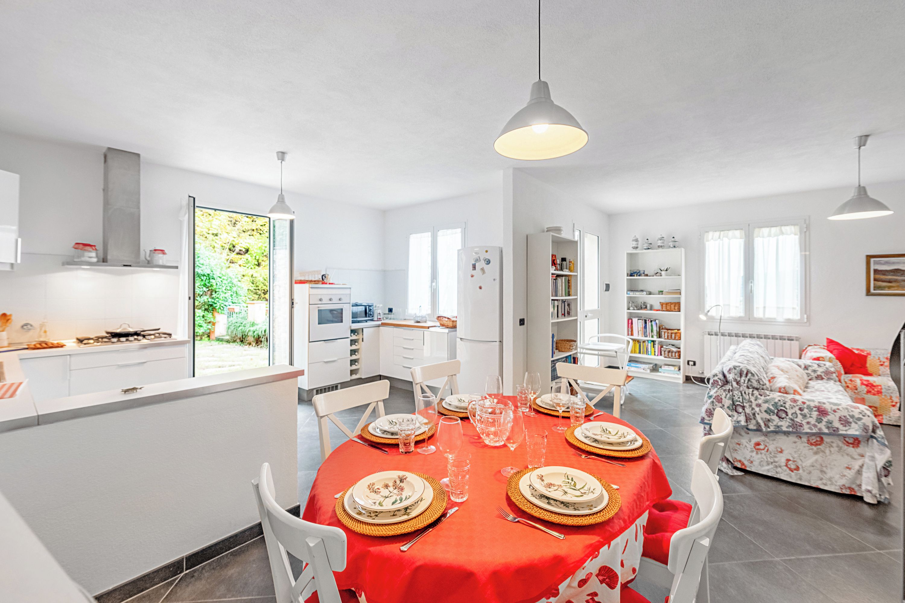A modern kitchen with white cabinets, a dining area with a red tablecloth, and a bedroom with floral bedding.