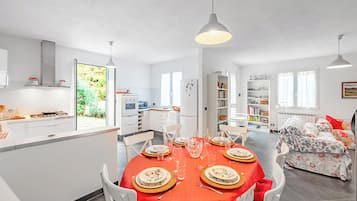 A modern kitchen with white cabinets, a dining area with a red tablecloth, and a bedroom with floral bedding.
