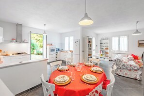 Una cocina moderna con armarios blancos, un comedor con mantel rojo y un dormitorio con ropa de cama estampada.