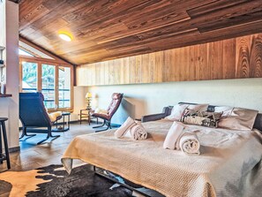 Ein gemütliches Zimmer mit Holzbalkendecke, einem Bett mit zusammengerollten Handtüchern, einem Sessel und Blick ins Freie.