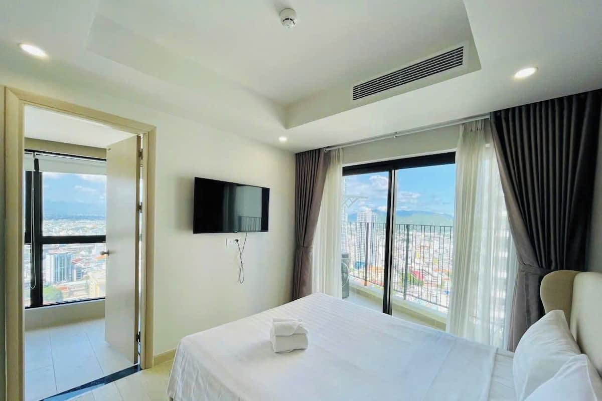 A hotel room with a large bed, a flat-screen TV mounted on the wall, and a balcony with a city view.