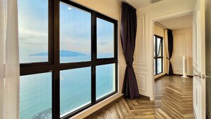 Un'ampia stanza con grandi finestre che si affacciano sul mare e sulla costa lontana. Il pavimento è in legno a parquet ed è presente un moderno climatizzatore.