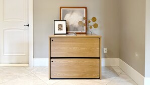 Un meuble en bois doté de deux tiroirs, une œuvre d’art abstraite encadrée et un élément décoratif en métal placé sur le dessus.