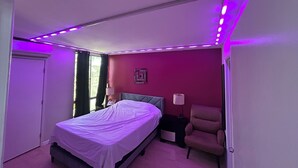 A bedroom with a bed, a chair, a nightstand, and a window with curtains.