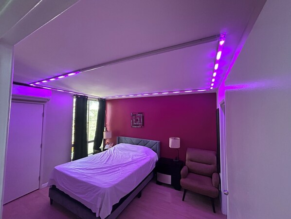 A bedroom with a bed, a chair, a nightstand, and a window with curtains.