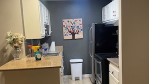 A kitchen with a central island, white cabinets, a painting of a tree, and a trash bin.