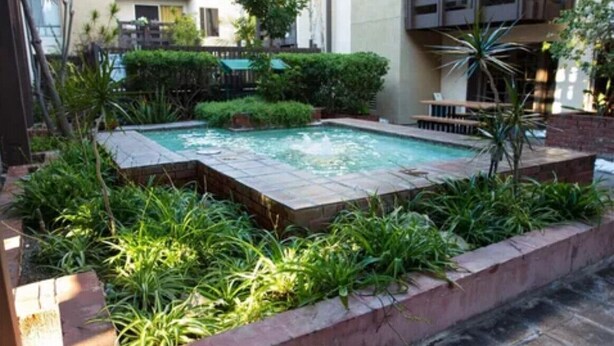 A rectangular pool with a fountain, surrounded by a brick border and lush greenery.