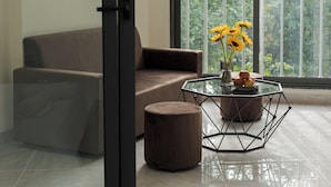 Un salon moderne avec un canapé marron, une table basse en verre dotée d’un pied géométrique et un petit pouf rond.