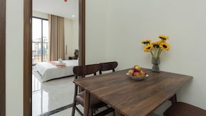 Une chambre d’hôtel avec une table à manger en bois, un vase rempli de tournesols et un saladier de pommes.
