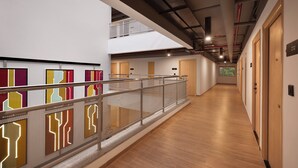 Een moderne hotelgang met een houten vloer, glazen balustrade en een entresol.