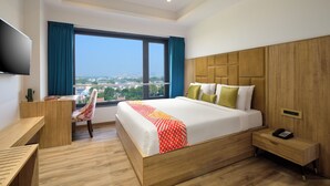 Een moderne hotelkamer met een groot bed, een bureau, een stoel, een televisie en uitzicht op de stad.