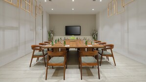 Een vergaderruimte met een lange tafel, stoelen, een televisie en decoratieve planten.