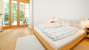 A bedroom with a wooden bed, a nightstand, a chair, and a view through a glass door to an outdoor area. - Talschluss 500 by Interhome (Saalbach-Hinterglemm)