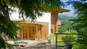 A modern outdoor patio with stone flooring, a wooden pergola, and a view of a forested valley. - Talschluss 500 by Interhome (Saalbach-Hinterglemm)