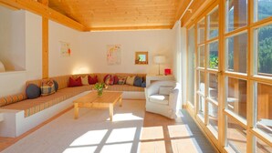 A spacious living room with a wooden ceiling, large windows, a sofa set, a coffee table, and a chair. - Talschluss 500 by Interhome (Saalbach-Hinterglemm)