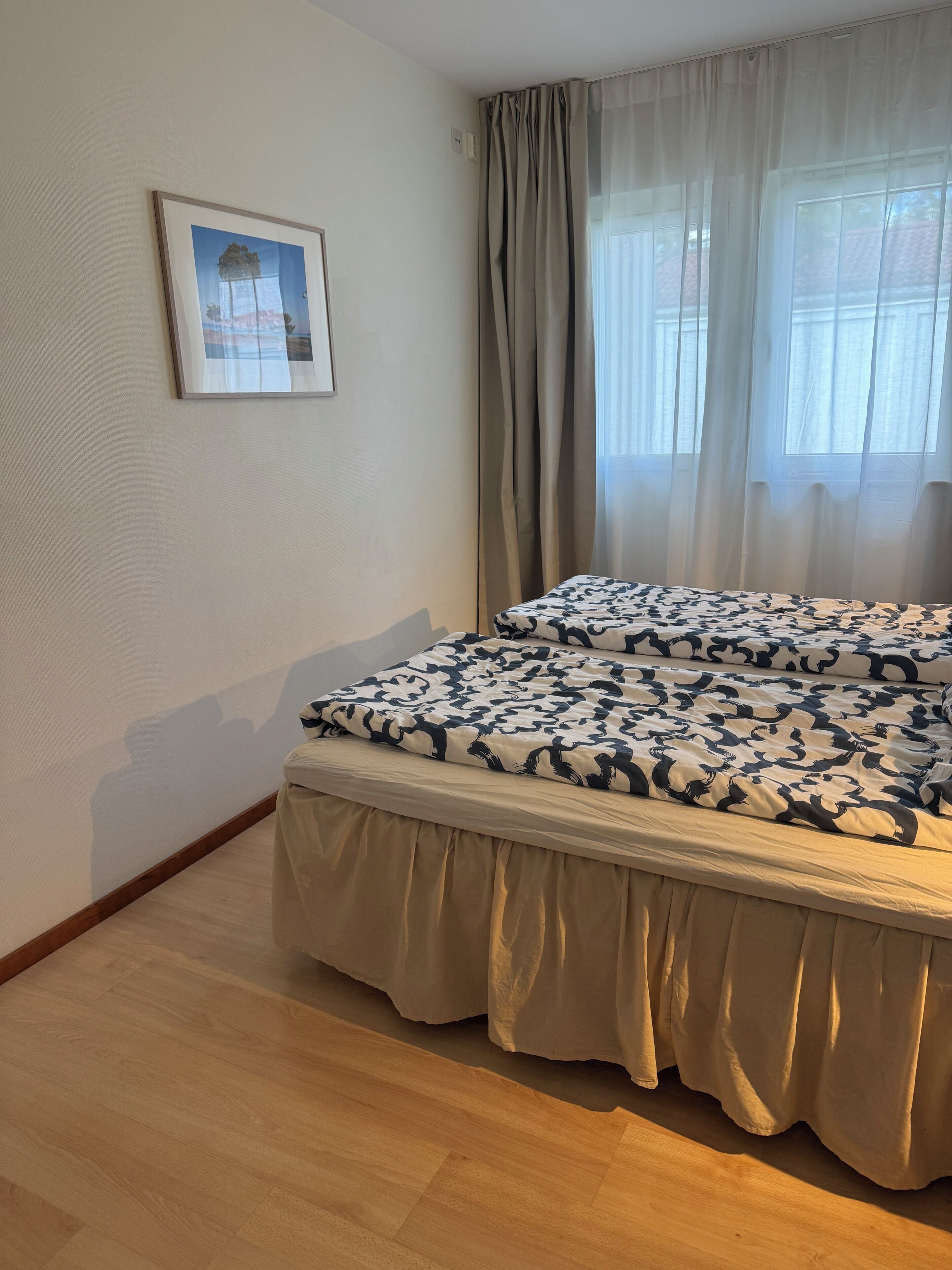 Ein Hotelzimmer mit Bett, einem Fenster mit Vorhängen, einem Wandbild und Holzboden.