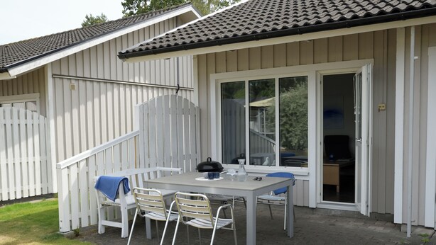 A patio with a table and chairs, a grill, and a sliding glass door leading to an indoor area. - Åhus Havsvillor (Aahus)