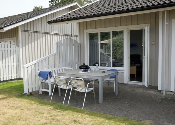 A patio with a table and chairs, a grill, and a sliding glass door leading to an indoor area. - Åhus Havsvillor (Aahus)