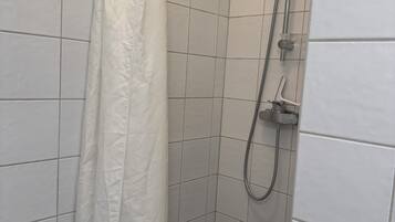 Ein Duschbereich mit weißer Duschvorhang, gefliesten Wänden und einer Handbrause.