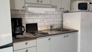 Una cocina con alacenas blancas, microondas, cafetera y estufa a gas.